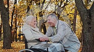 Caucasian senior man holding female hand caring woman with disability on wheelchair husband accompanies sick wife during