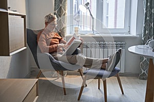 Caucasian senior man relaxing at the armchair at home while reading his favorite book