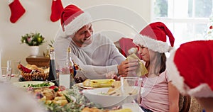 Caucasian senior man in santa hat wiping his daughter face with tissue sitting on dining table and e