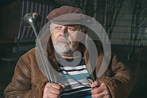 Caucasian senior man sitting next to his house with horn at cold autumn night