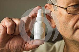 Caucasian senior man uses an ear spray. Man& x27;s hand holds a white ear spray bottle with nozzle installed in the ear