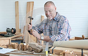 Caucasian senior old white bearded man carpenter using hammer and chisel working in workshop, tools machine small wooden toy model