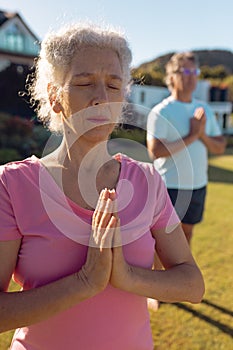 Caucasian senior woman and man meditating in prayer position in yard at retirement home