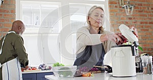 Caucasian senior woman wearing apron putting vegetable peelings in a compost bin in the kitchen