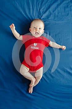 Caucasian smiling baby boy girl with blue eyes lying on bed at home on Canada Day