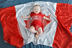 Caucasian smiling baby boy girl with blue eyes lying on large Canadian flag with red maple leaf