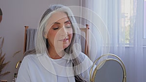 Caucasian smiling beautiful old senior lady mature aging elderly model woman with gray hair female looking at mirror