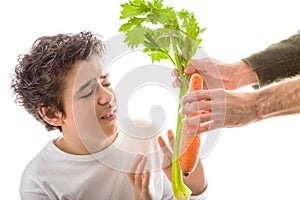 Caucasian smooth-skinned boy holds hands to reject carrot and ce