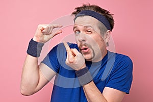 Caucasian sportive man show small size by fingers demonstrate tiny measure