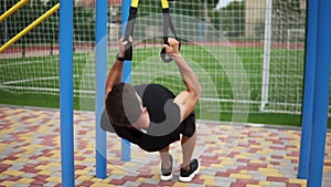 Caucasian sportsman doing pull ups exercise using fit belt to force strenth of workout outdoors