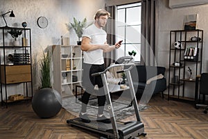 Caucasian sportsman having online video class training on smartphone using treadmill