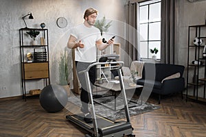 Caucasian sportsman having online video class training on smartphone using treadmill