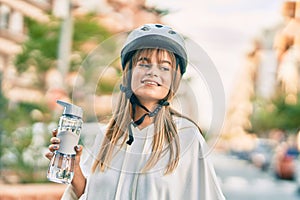 Caucasian sporty teenager girl wearing bike helmet and drinking bottle of water at the city