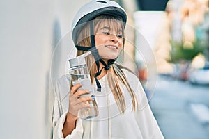Caucasian sporty teenager girl wearing bike helmet and drinking bottle of water at the city