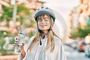 Caucasian sporty teenager girl wearing bike helmet and drinking bottle of water at the city