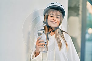 Caucasian sporty teenager girl wearing bike helmet and drinking bottle of water at the city