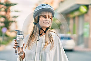 Caucasian sporty teenager girl wearing bike helmet and drinking bottle of water at the city