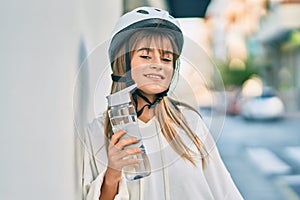 Caucasian sporty teenager girl wearing bike helmet and drinking bottle of water at the city