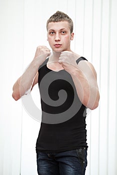 Caucasian strong blond man stands in boxing pose on white background, black gym shirt