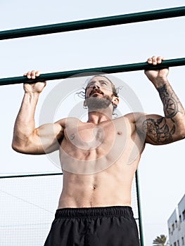 Caucasian strong man doing pull ups outdoor at the park