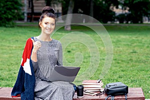 Caucasian student girl is using laptop and shows thumb up at the park