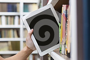 Caucasian student putting digital tablet on bookshelf