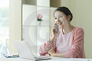 Caucasian successful businesswoman talking on phone and working on laptop computer at home office