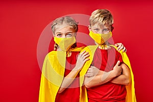 Caucasian superheroes kids in medical masks isolated on red background