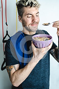 Caucasian tattooed man eating notorious oatmeal bowl after training at home. Fitness and wellbeing concept photo