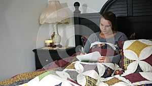 A Caucasian teacher grading papers in her bed at night - the class is failing