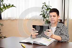 Caucasian teen boy learning language online using digital tablet, doing school tasks at home. E-learning concept