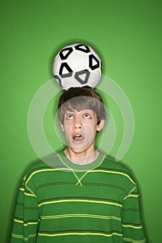 Caucasian teen boy with soccer ball on head.