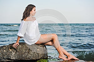 Caucasian teen girl in bikini and white shirt lounging on lava rocks by the ocean