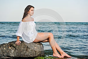 Caucasian teen girl in bikini and white shirt lounging on lava rocks by the ocean