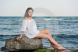 Caucasian teen girl in bikini and white shirt lounging on lava rocks by the ocean