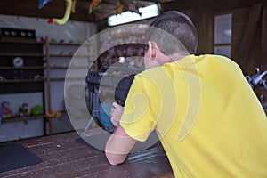 Caucasian teenage boy aiming with black pneumatic rifle in a shooting galery, rear view photo