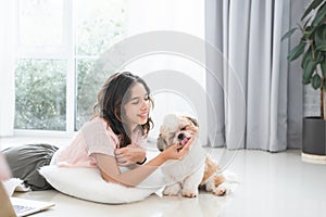 Caucasian teenage girl playing with shih tzu puppy dog at home with love. Young woman lying on floor, feeding food to