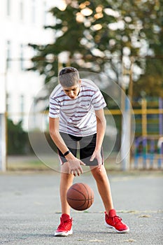 Caucasian teenager boy with a ball on outdoor city court. Basketball player practicing and posing for the shoot.