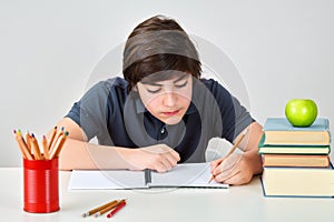 Caucasian teenager boy sitting at the table writing to his notebook.