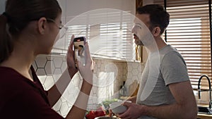 Caucasian teenager girl recording her father during the cooking.