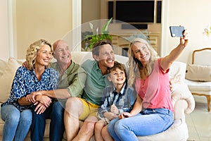 Caucasian three generation family taking a selfie while sitting together on couch at home