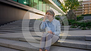 Caucasian tired business woman mature old senior sick unwell businesswoman on city stairs rest overwork hard day