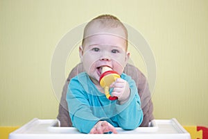 Caucasian toddler baby 5 6 months boy girl sits on a high chair and eats fruit from a nibbler. kid child learns to eat