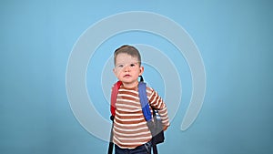 Caucasian toddler boy with a backpack on a blue background. Little schooler