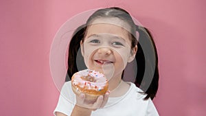 Caucasian toddler girl with ponytails holds pink donut, smiles and looks at the camera. Healthy organic homemade food