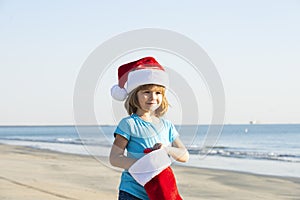 Caucasian toddler kid in santa hat on the beach. Traveling on holidays. Christmas child.