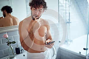 Caucasian topless man texting while brushing teeth