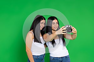 Caucasian twin girls take pictures with a vintage camera. Green background, side space.