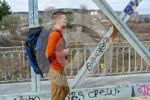 Caucasian white man with an orange sweater and a backpack walking on the bridge
