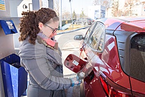 Caucasian white woman at gas station, unscrews the fuel cap of her car to refuel